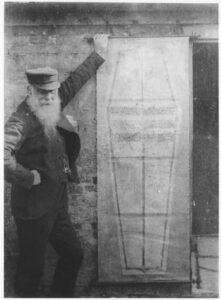 Victorian photo of a man with a beard holding up a long piece of paper